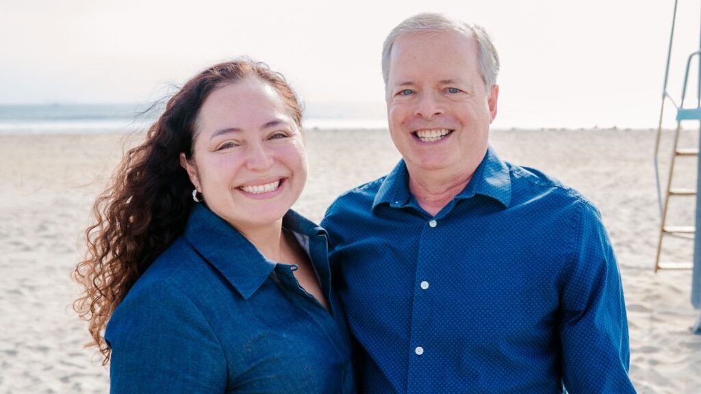 A woman and man dressed in blue shirts and standing in the beach. 